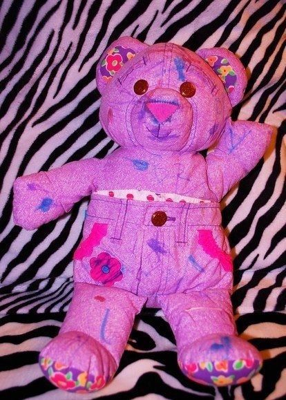 a pink teddy bear sitting on top of a zebra print bed sheet with paint splattered all over it