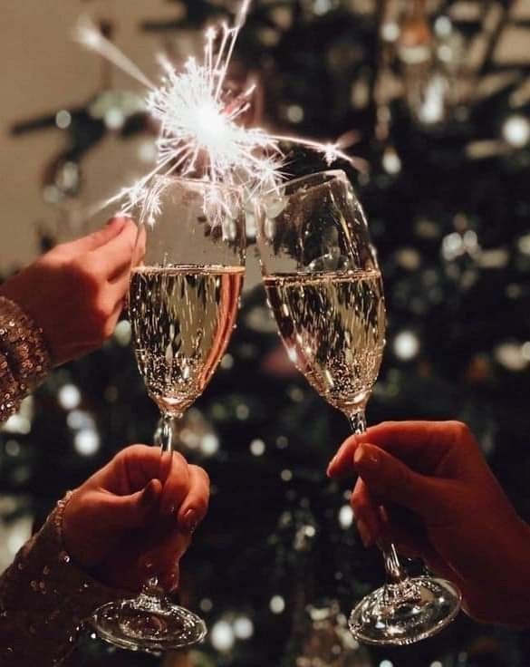 two people are toasting with champagne glasses in front of a christmas tree that has lights on it