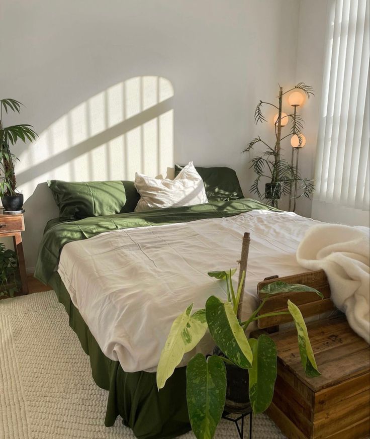 a bedroom with white walls, green bedding and potted plants on the floor