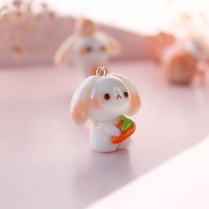 a small white rabbit figurine holding a carrot in it's mouth on a pink surface