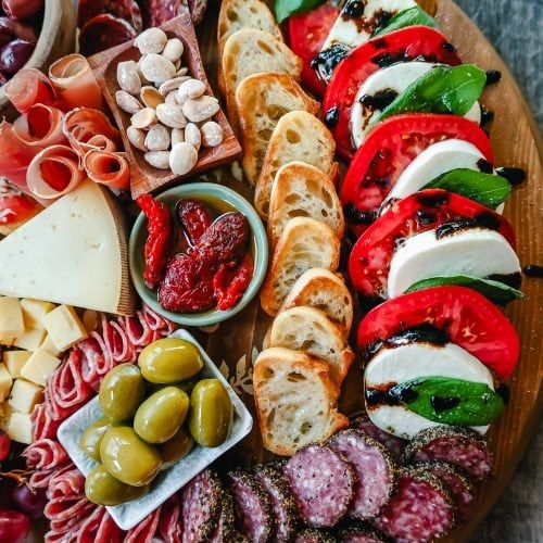 a platter filled with meats, cheeses and olives next to other foods