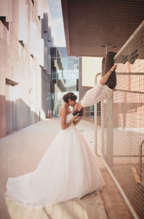 a bride and groom kissing in front of a metal fence on their wedding day at the same time