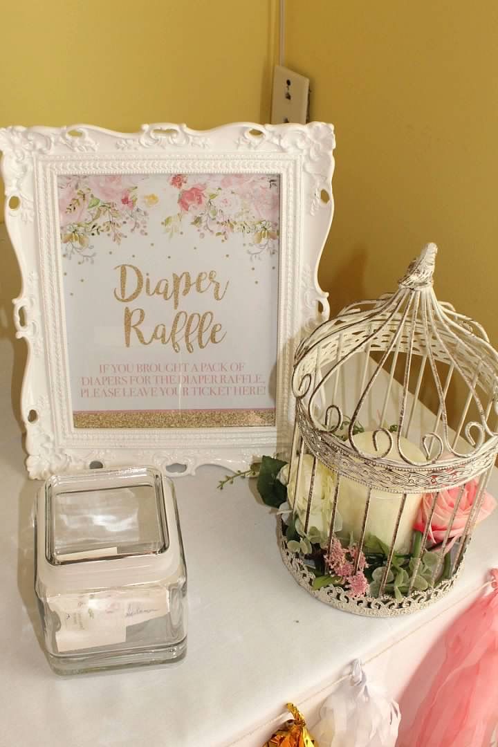 a white birdcage sitting on top of a table next to a sign that says diaper raffle