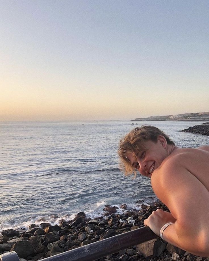 a shirtless man leaning on a rail next to the ocean with his head down