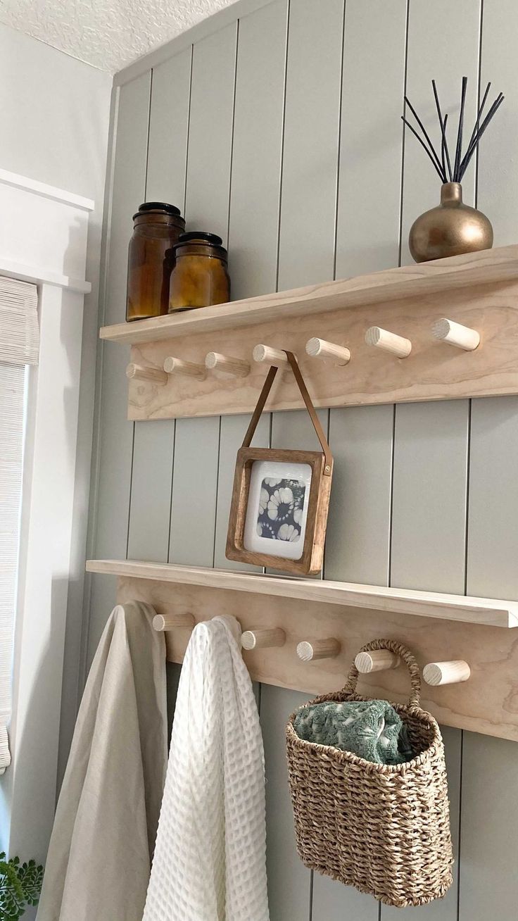 two wooden shelves with hooks and baskets on them next to towels hanging from the wall