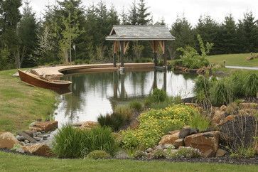 a gazebo in the middle of a pond surrounded by grass and rocks, with trees around it