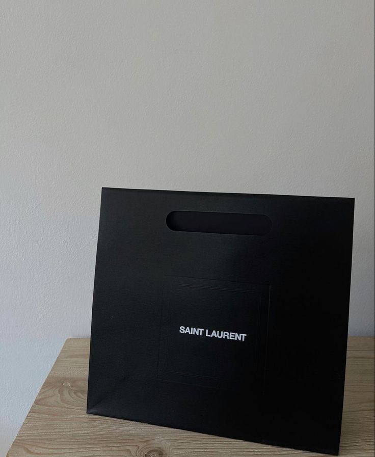 a black shopping bag sitting on top of a wooden table next to a white wall