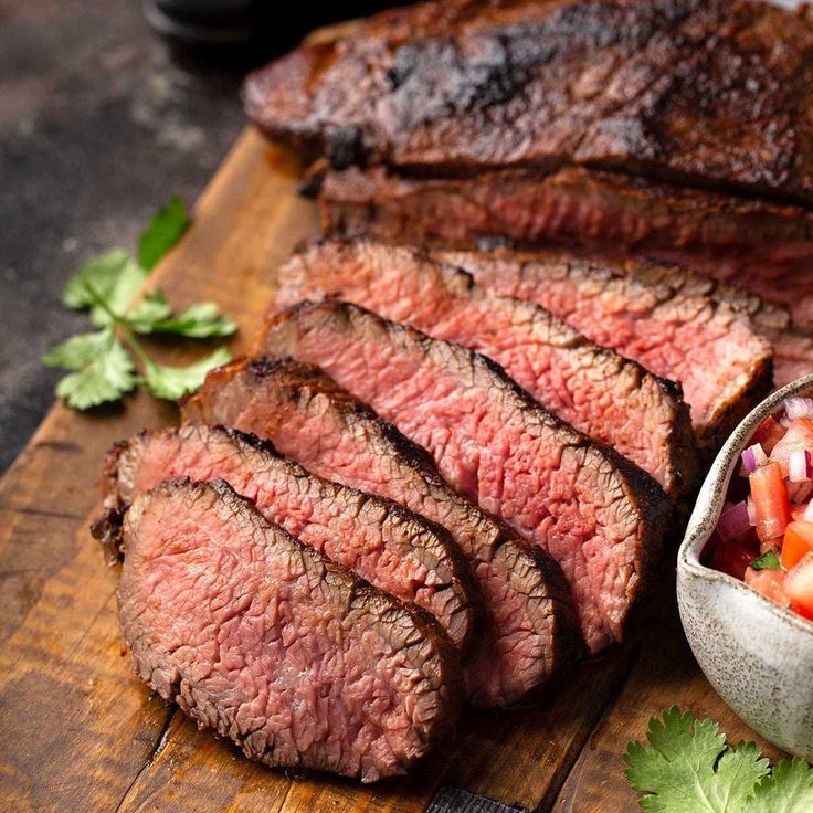 sliced steak on cutting board with garnishes and knife next to it, ready to be served