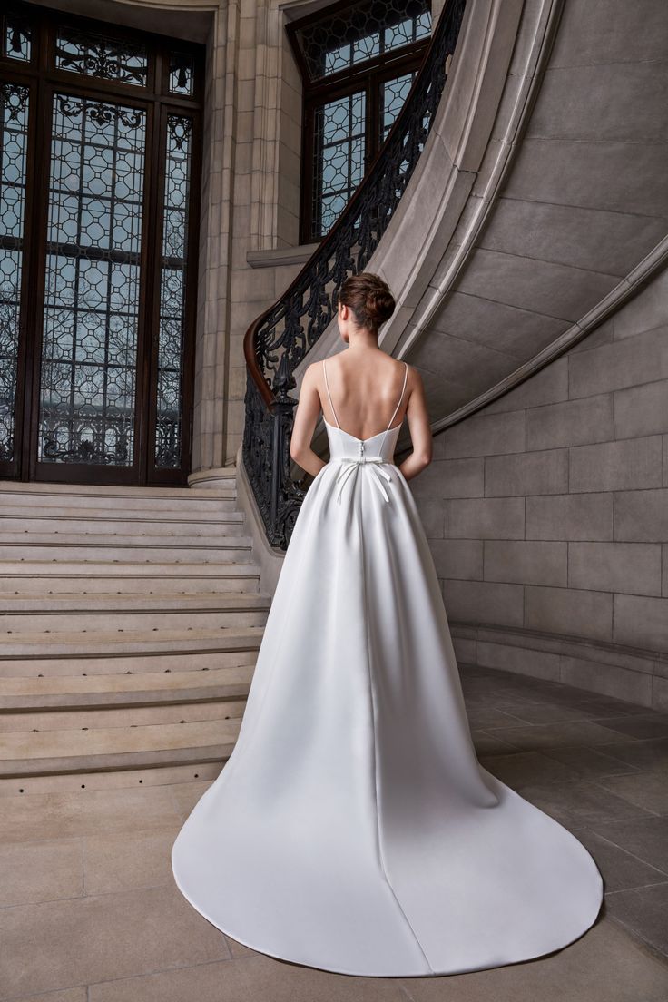 a woman in a white wedding dress standing at the top of some stairs with her back turned to the camera