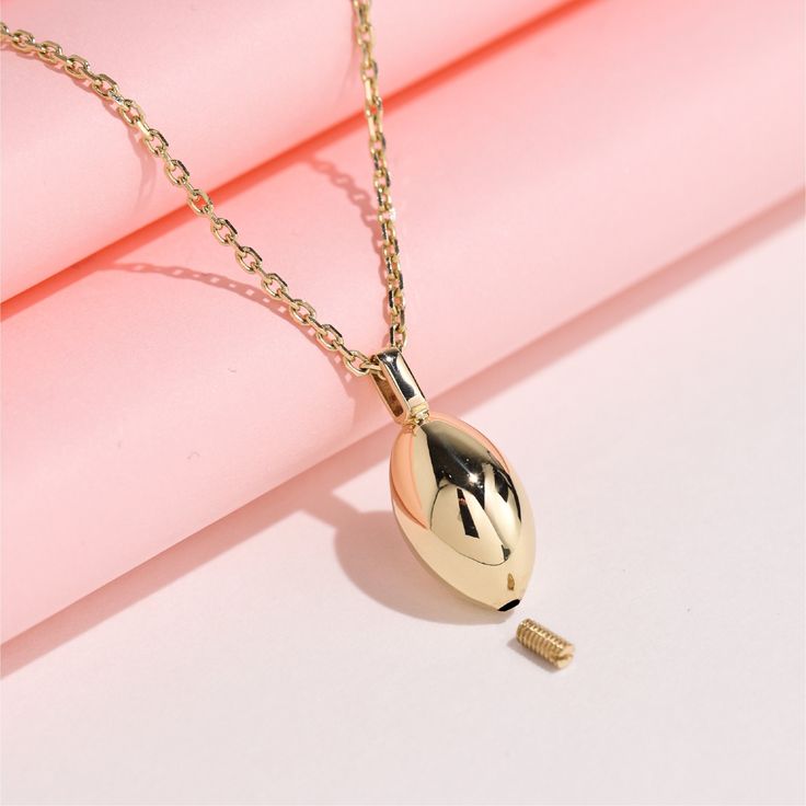 a gold necklace with a black and white ball hanging from it's end on a pink surface