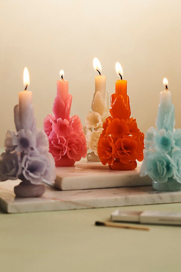 five candles with different colored flowers on them next to a notebook and pencils in the background