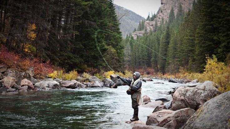 a man standing on top of a river while holding a fishing rod in his hand