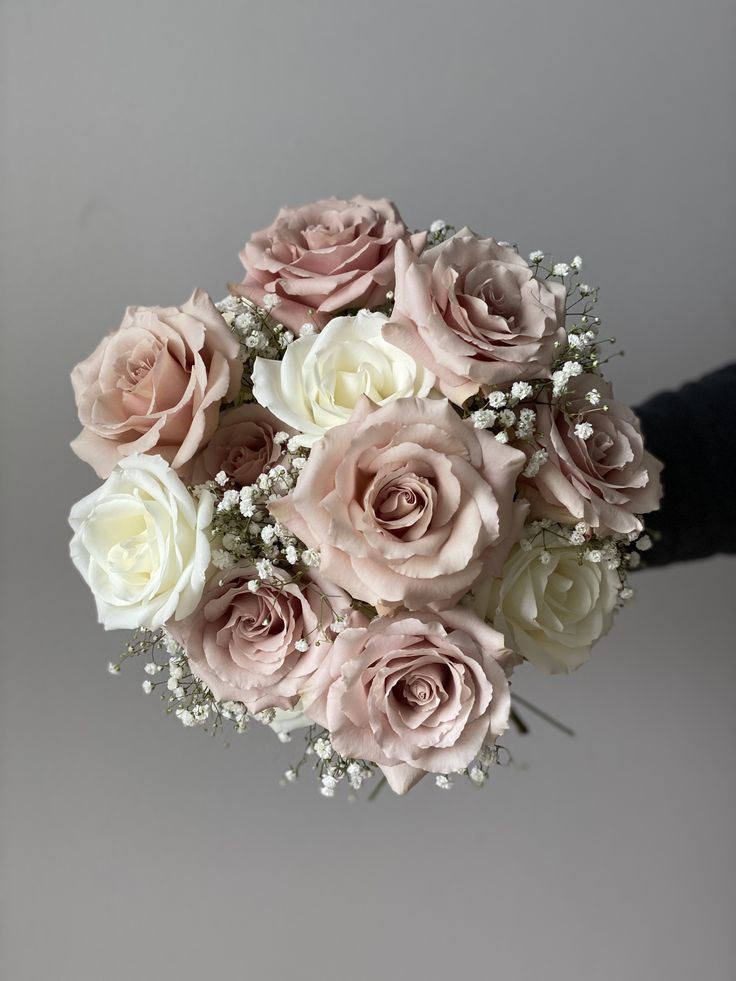 a bouquet of pink and white roses is held by someone's hand on a gray background