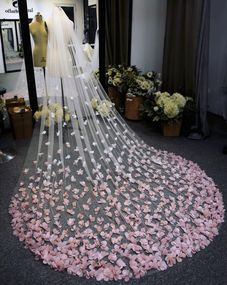 a wedding dress with pink flowers on the bottom and veil hanging from it's side