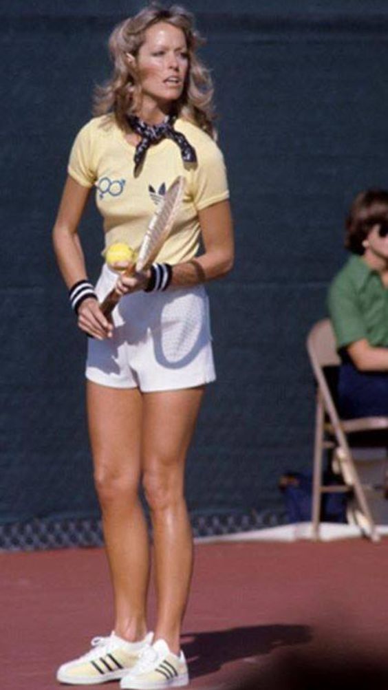 a woman holding a tennis racquet on top of a tennis court with people sitting in chairs behind her