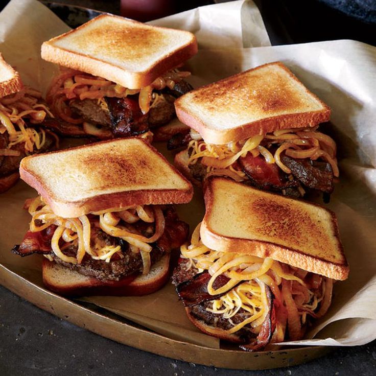 four sandwiches with cheese and meat on them in a basket, ready to be eaten