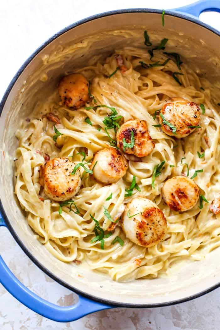 pasta with scallops and parsley in a blue pot on a white table