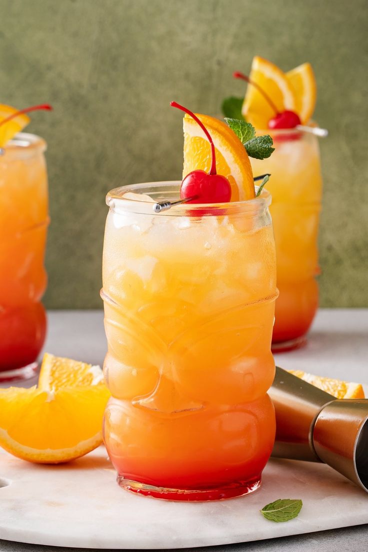 two glasses filled with orange juice and garnished with cherries on the rim