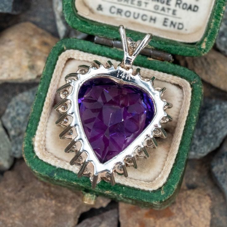 This gorgeous heart shaped pendant is centered with one (1) heart mixed cut amethyst set into a eight-prong setting. The center stone is bordered with twenty-four (24), prong set, round brilliant cut diamonds. The split "V" shaped bail is accented with one (1), prong set, round brilliant cut diamond. The pendant measures 29.7mm X 21.6mm X 12.6mm. This pendant does not include a chain. Heart Cut Hallmarked Collectible Jewelry, Heart Cut Purple Jewelry With Accent Stones, Purple Heart Cut Jewelry With Accent Stones, Antique Heart Cut Jewelry For Formal Occasions, Vintage Purple Heart-shaped Jewelry, Heart Cut Amethyst Jewelry With Center Stone, Purple Heart Cut Jewelry For Formal Occasions, Purple Heart Cut Jewelry For Formal Events, Purple Heart Jewelry For Formal Occasions