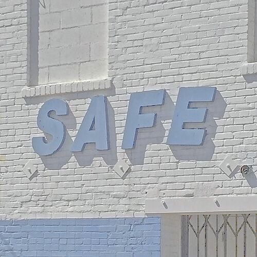 a white brick building with the word safe painted on it's side and an orange fire hydrant in front