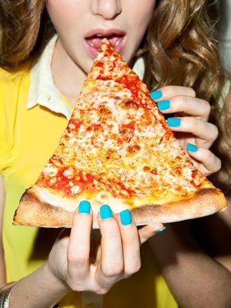 a woman holding a slice of pizza in front of her face and making a funny face