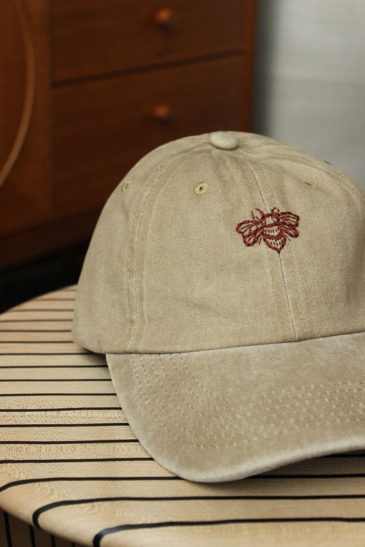 a baseball cap with a bee embroidered on it sitting on top of a wooden table