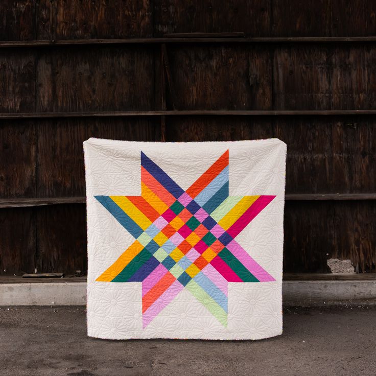 a multicolored star quilt hanging on a wooden wall