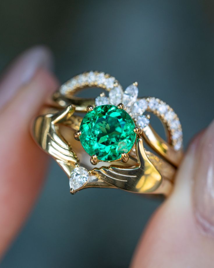 a close up of a person's hand holding a ring with a green stone