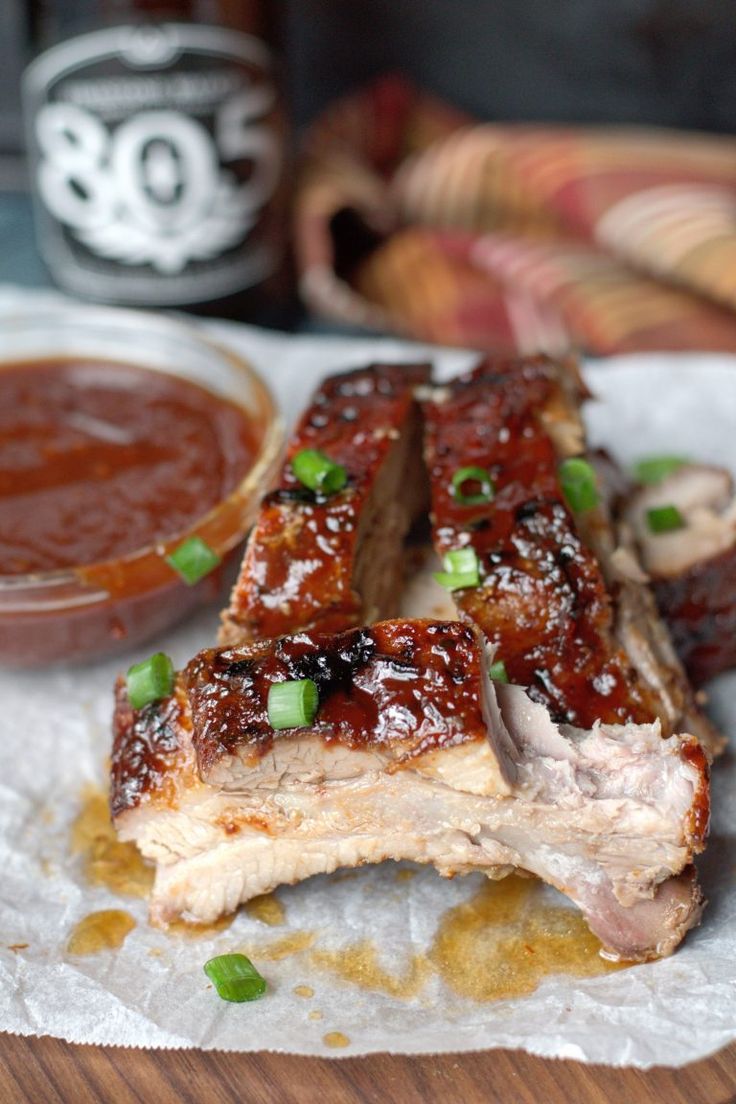 barbecue ribs with sauce and green onions on a napkin next to some dipping sauces