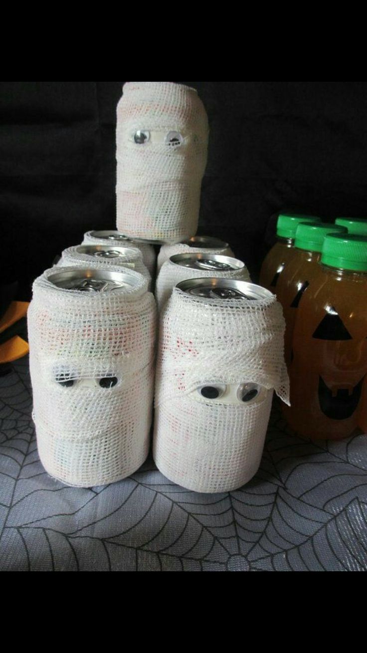 there are four jars wrapped in white paper with faces on them and two pumpkins behind them