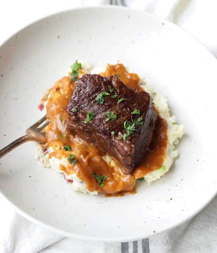 a white plate topped with meat and mashed potatoes covered in gravy, garnished with parsley