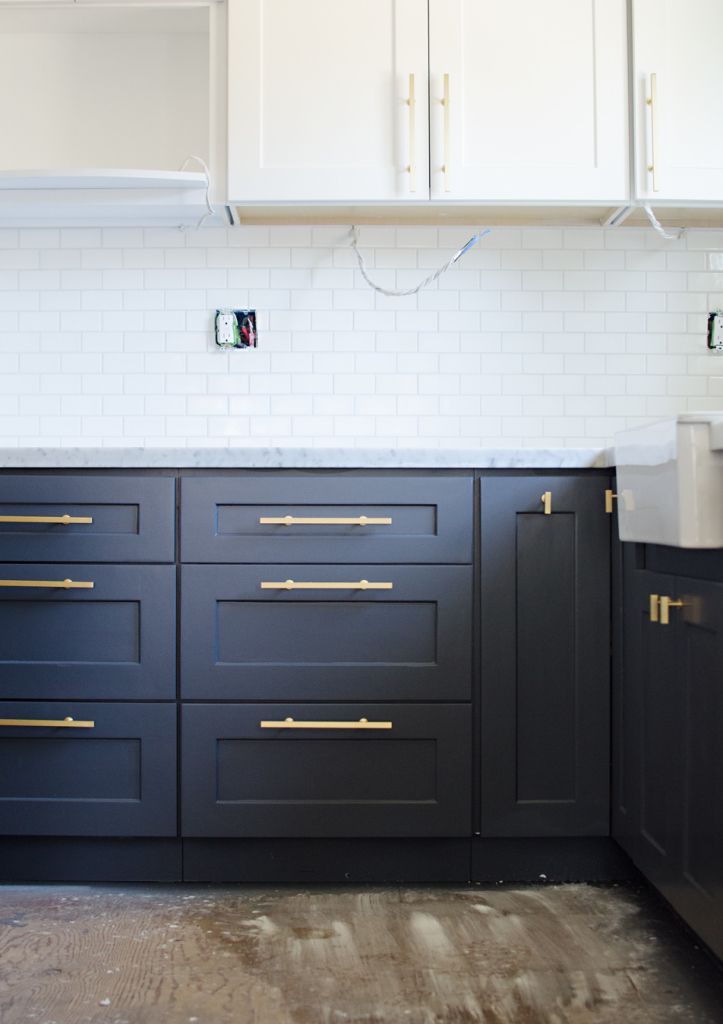 a kitchen with black cabinets and white subway backsplash, gold pulls on the cabinet doors