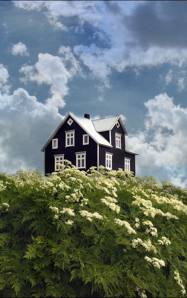 a black and white house sitting on top of a lush green hillside under a cloudy blue sky