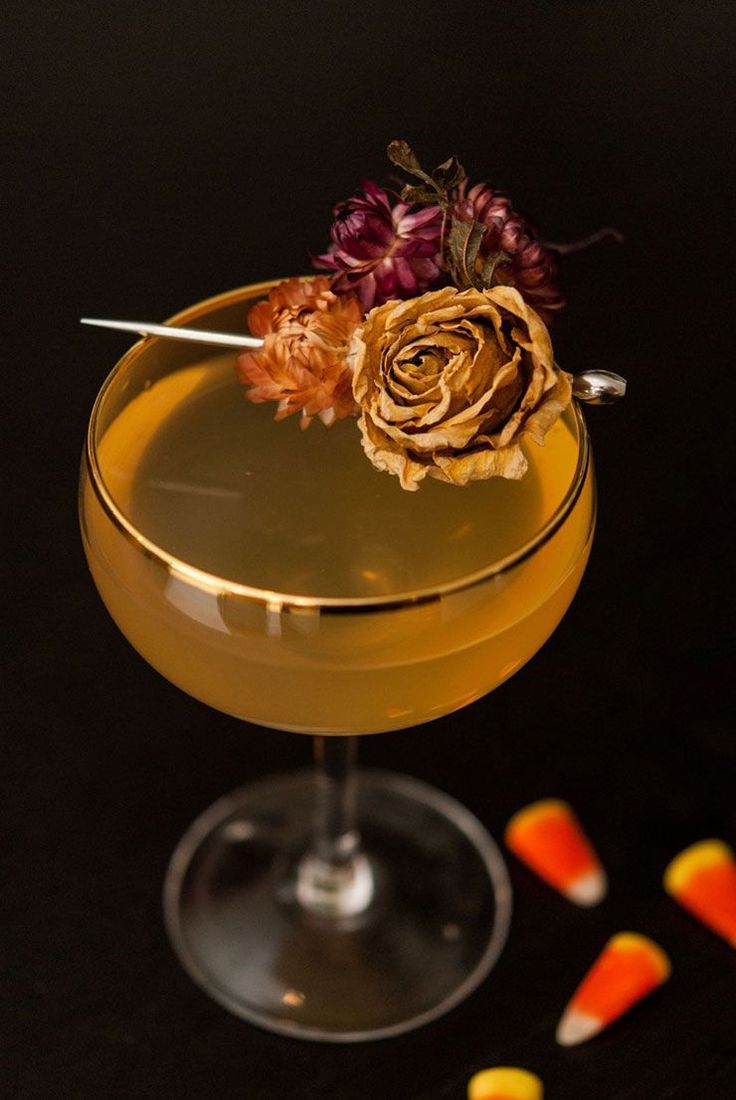 a yellow cocktail in a glass with candy on the side and a flower sticking out of it