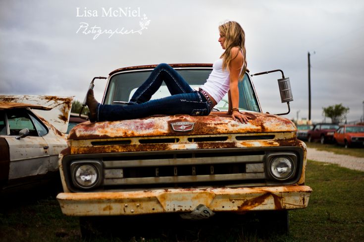 a woman sitting on the hood of an old pickup truck with rusted out paint