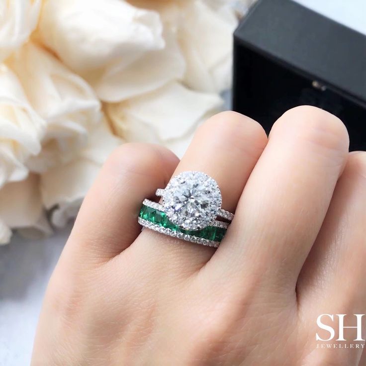 a woman's hand holding a diamond and emerald ring