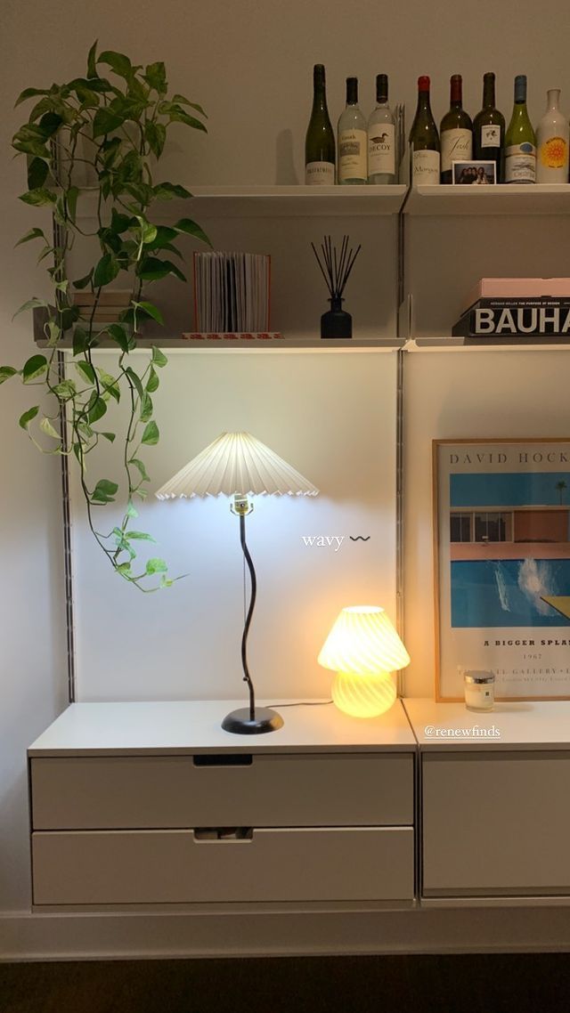 a lamp is sitting on top of a dresser next to a shelf filled with bottles