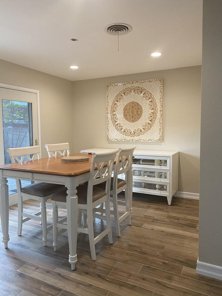 a dining room table with four chairs and a painting on the wall