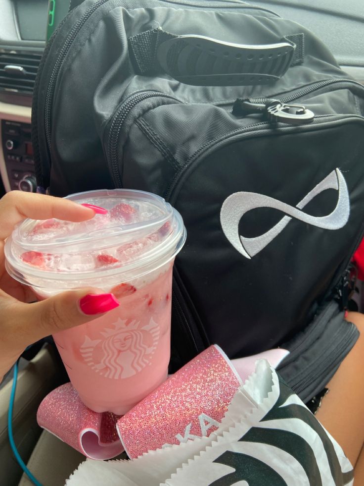 a person holding a cup with pink liquid in it next to a backpack and purse