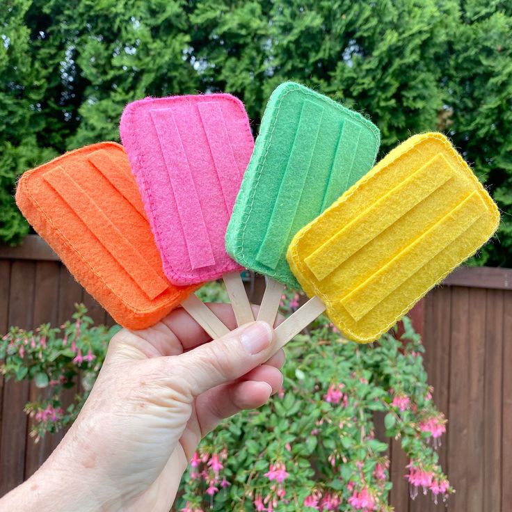 a hand holding four popsicles in different colors