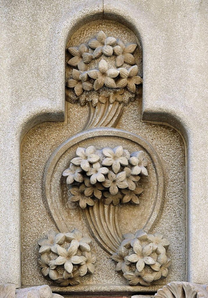 an ornate design on the side of a building with flowers growing out of it's center