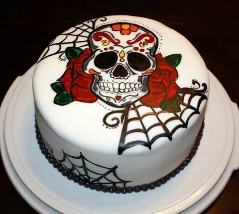 a white cake with a sugar skull and red roses on the top is sitting on a plate