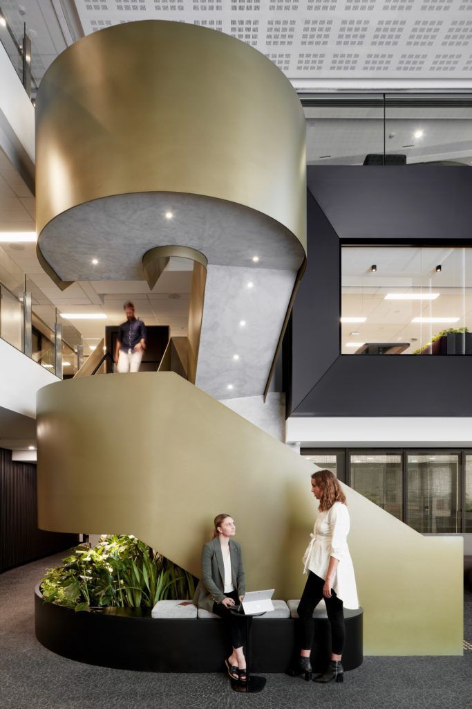 two people are sitting on a bench in an office building with stairs leading up to the second floor