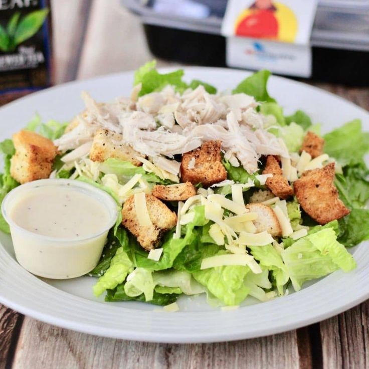 a white plate topped with lettuce and croutons next to a container of ranch dressing