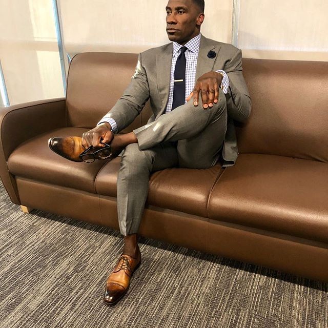 a man in a suit and tie sitting on a brown leather couch with his feet up