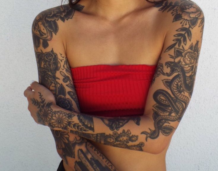 a woman with tattoos on her arms and chest posing for the camera while wearing a red top