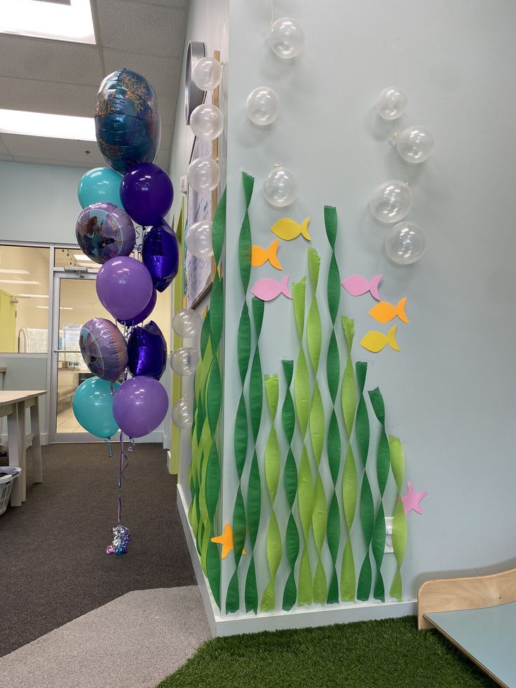 an office decorated with balloons and fish on the wall, along with fake grass in the floor