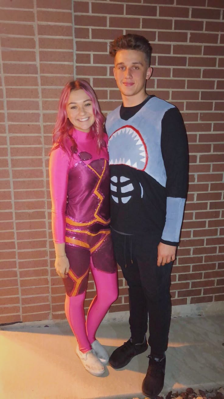 a young man and woman dressed up in costumes standing next to each other near a brick wall