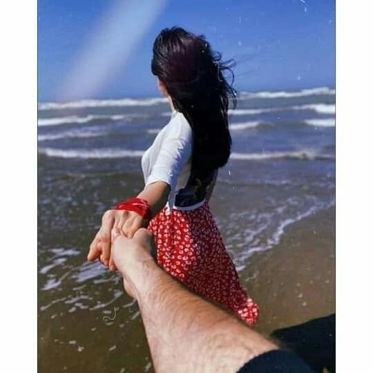 a man holding the hand of a woman on top of a sandy beach next to the ocean