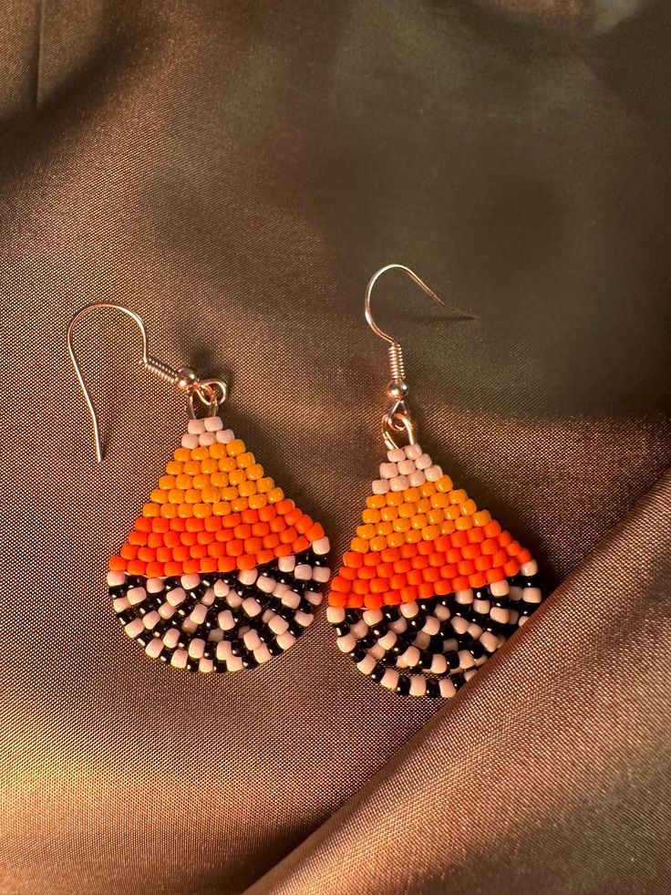 a pair of orange and black beaded earrings sitting on top of a piece of fabric